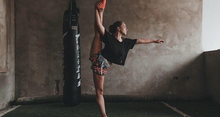 Athlete in a standing split beside a punching bag in a gym