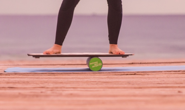 Barefoot athlete balancing on a balance board on a wooden dock by the water.