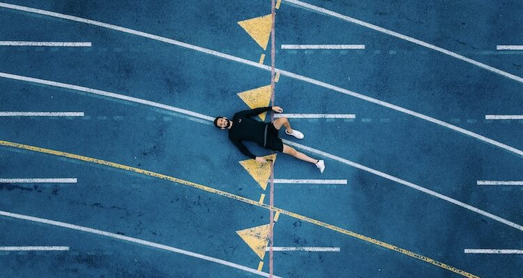 Athlete lying on his back on a running track, taking a moment to reset and recover from mistakes in sports