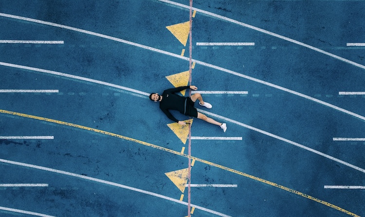 Athlete lying on his back on a running track, taking a moment to reset and recover from mistakes in sports