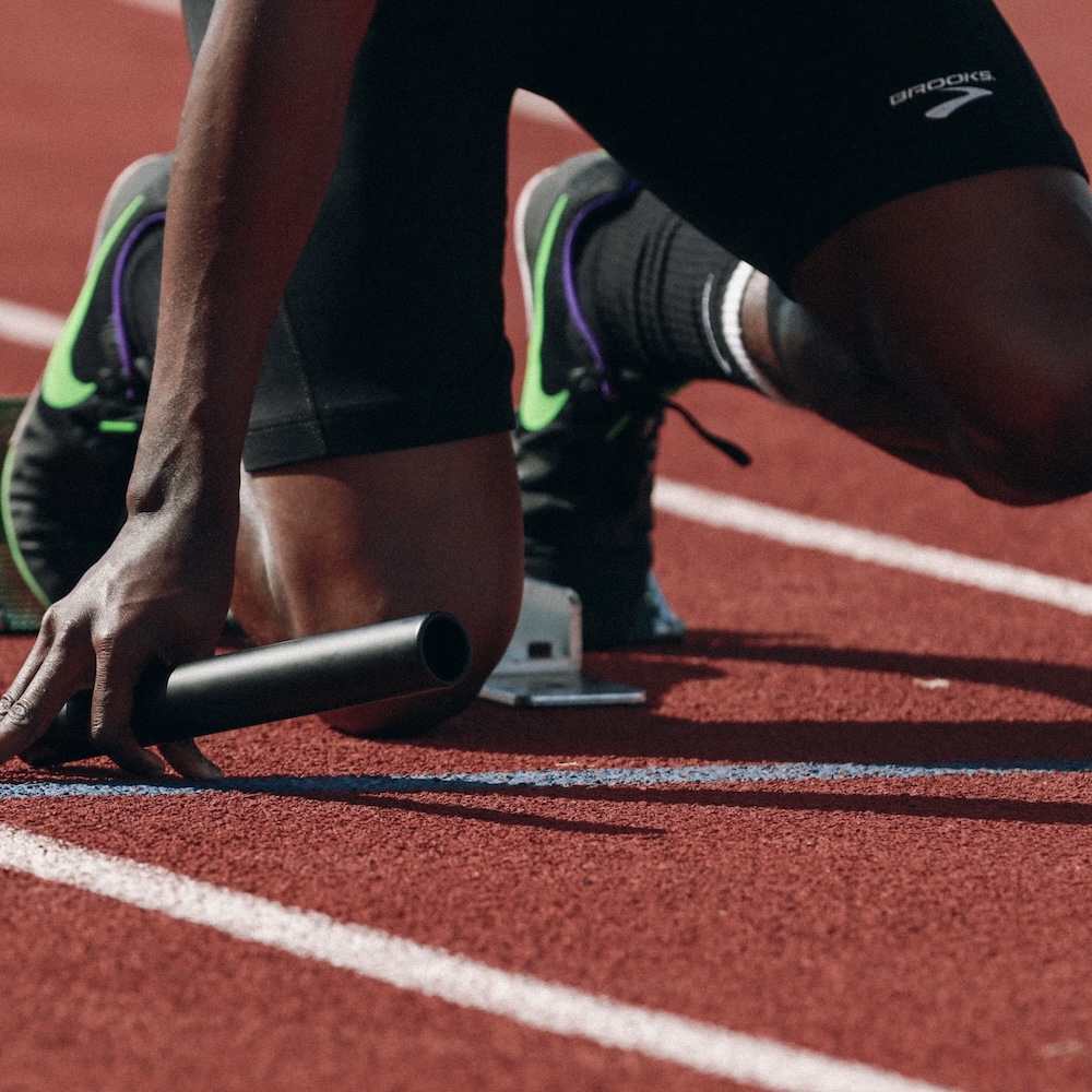 runner in starting blocks on track with a relay baton in right hand 