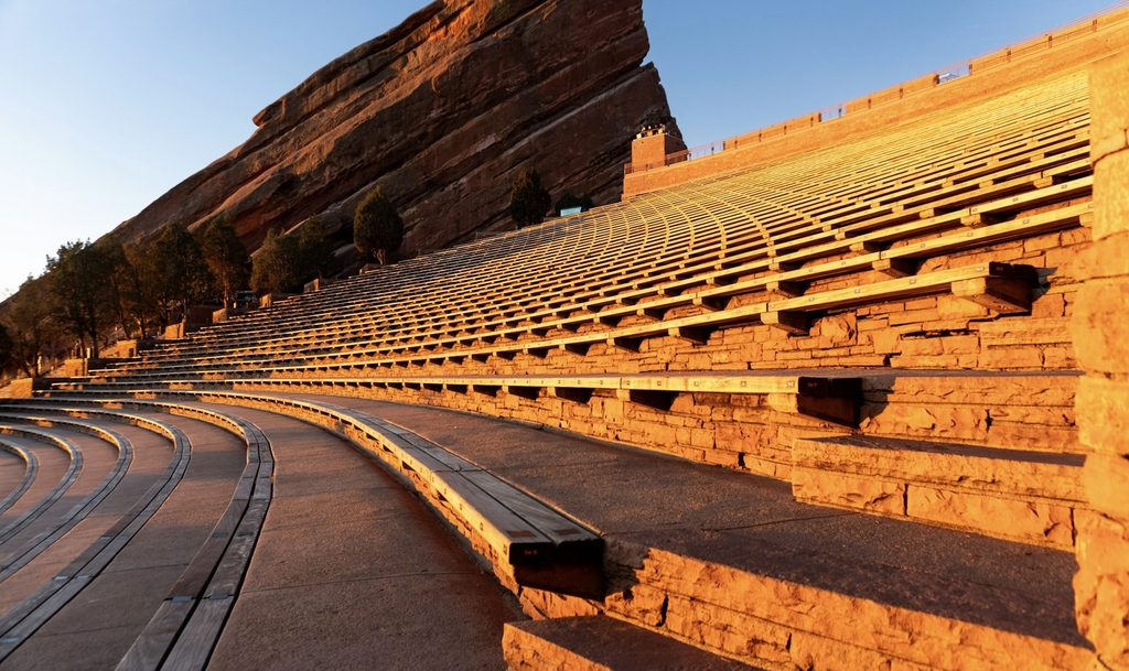 Empty rows of seating at Red Rocks Amphitheatre glowing in golden light beneath a towering sandstone monolith, one of the most memorable fall activities in Denver